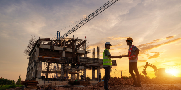 Two engineers in a building site shaking hands with the sunset behind them.