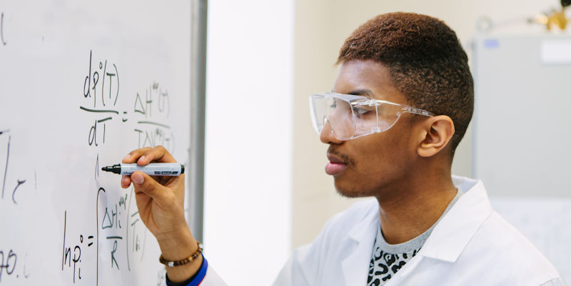 Male UG student writing on whiteboard in chemical engineering teaching lab