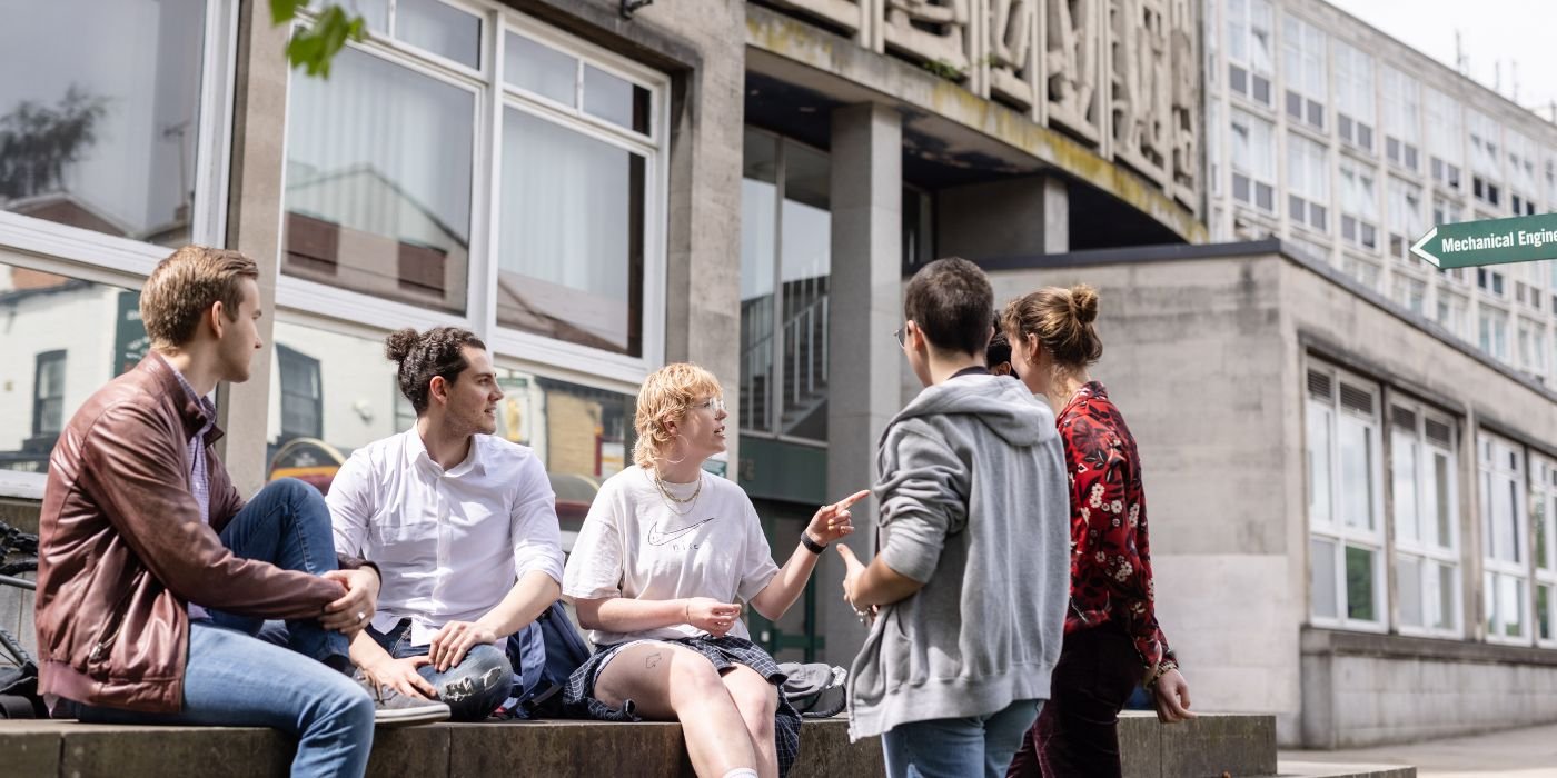 A group of students sat outside on a wall in front of the School of Mechanical Engineering.