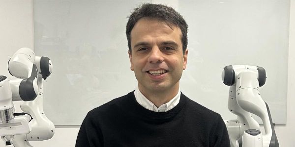 Professor mehmet dogar standing in front of a whiteboard and two robotic arms