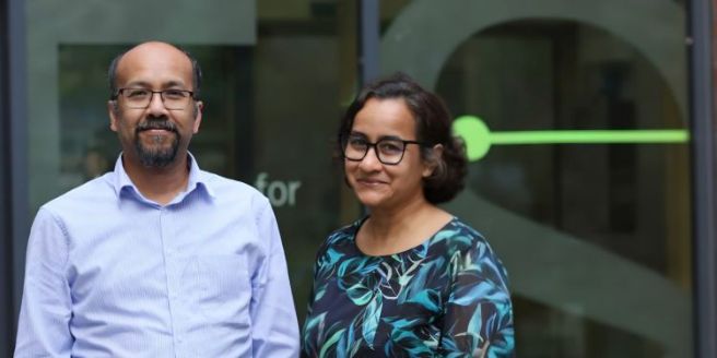 Image of a man wearing light blue shirt and glasses next to a woman wearing a blue top with green leaves smile at the camera