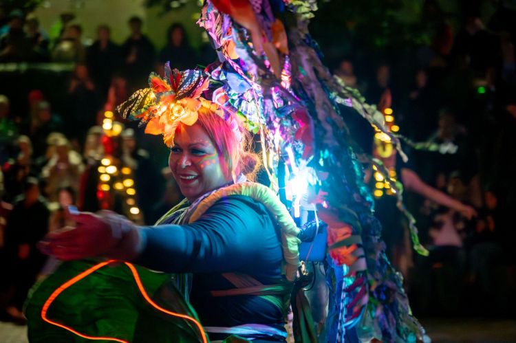 Mama Mycelium, the centrepiece costume for the Banyan performance, being worn by a smiling woman dancing in front of a crowd.