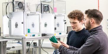 A student and a technician talking through the product created by a 3D printer in the School of Mechanical Engineering.