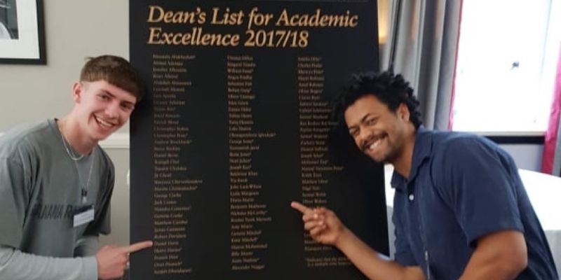 Benjamin Matheson and a fellow course mate stood next to the Dean's List board pointing to their names.