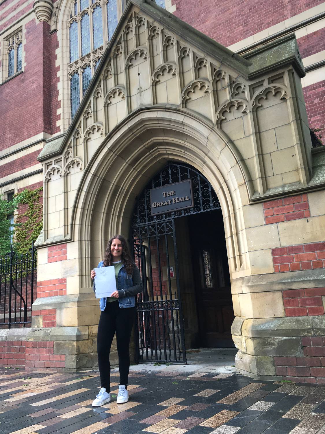 Holly Dimmick standing in front of a university building holding her dissertation
