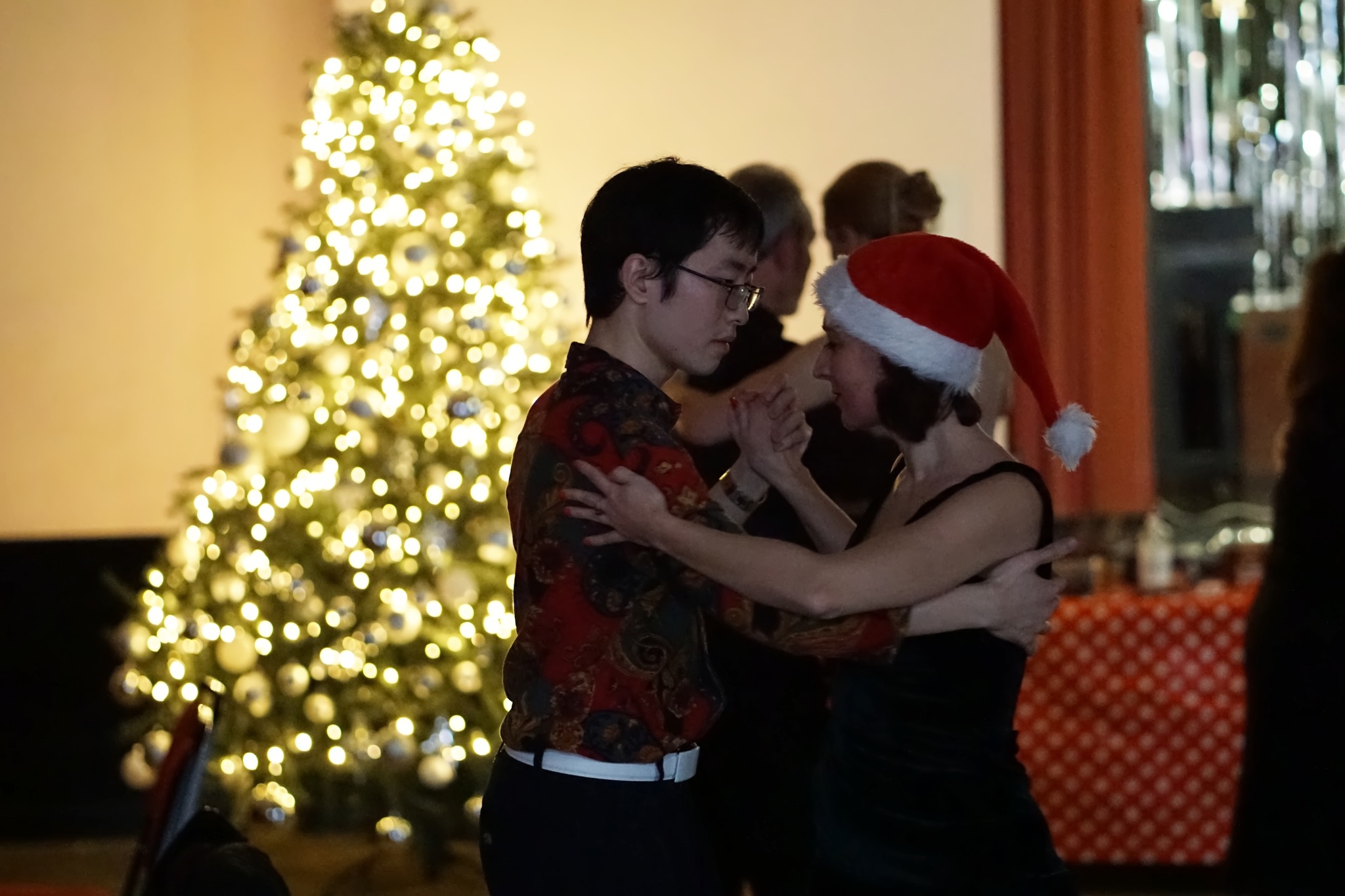 Muyou Li and a female student are dancing an argentine tango in front of a christmas tree