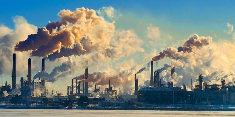 Industrial refinery with multiple smokestacks releasing thick clouds of smoke and steam into the sky, symbolising air pollution and environmental impact.