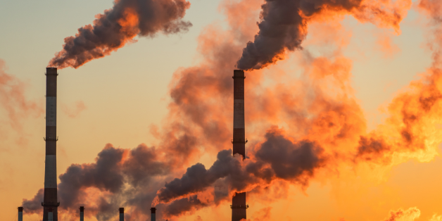 Industrial plants release emissions into a sunset sky.