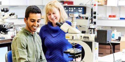 Professor Helen Gleeson and School of Physics and Astronomy colleague Dr Devesh Mistry looking at a microscope and smiling.