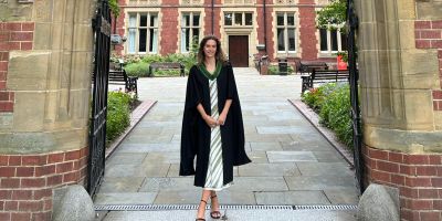 Jo Morton wearing her graduation gown standing under the great hall archway