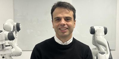 Professor mehmet dogar standing in front of a whiteboard and two robotic arms