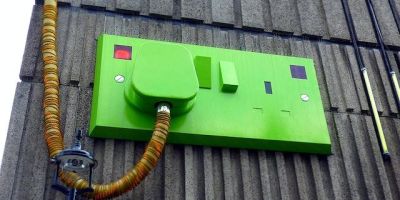 A British double plug socket with a plug in one socket, all painted green