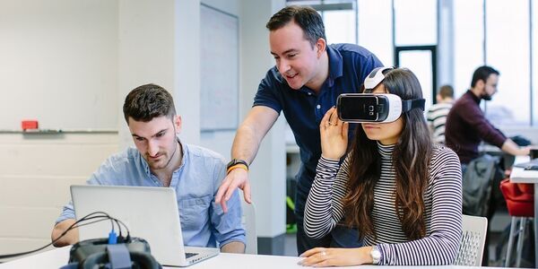 Three Computing students, one using VR