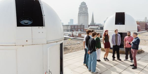 A group of students listening to an academic on the roof of the Sir William Henry Bragg Building, in between two observatories.