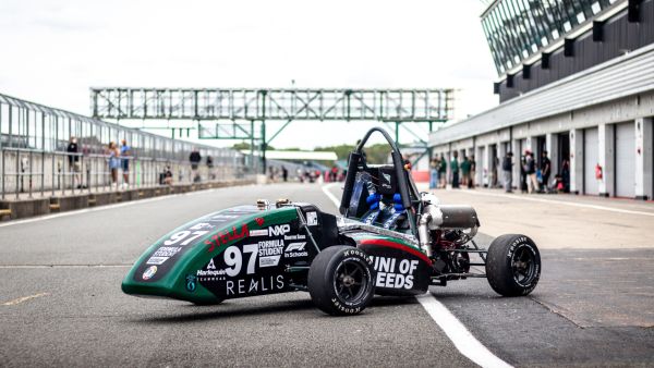 A racing car with University of Leeds branding, parked at an angle in a pit lane.