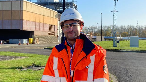 Reece wearing a safety helmet and orange jacket onsite at national grid