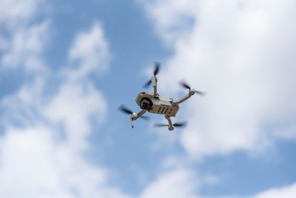A generic UAV drone flying in the blue sky, with a scattering of clouds