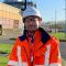 Reece wearing a safety helmet and orange jacket onsite at national grid