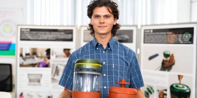 A Product Design student showing his project work, holding up a prototype to camera, with his poster blurred in the background.