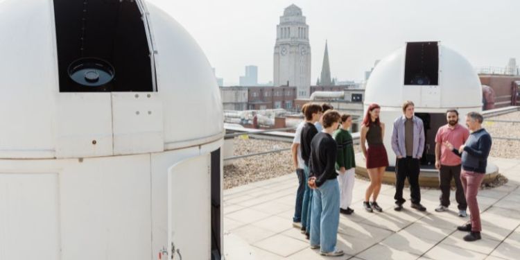 A group of students having a introduction to the observatories from an academic on the roof of the Sir William Bragg Building.