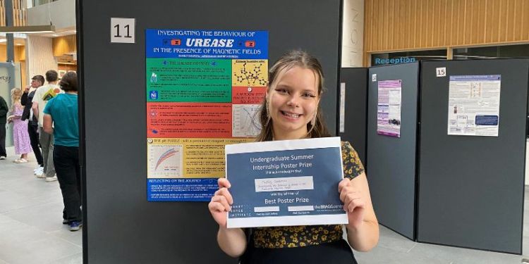 A portrait of Nelly Sadarova in front of a research poster holding a certificate.