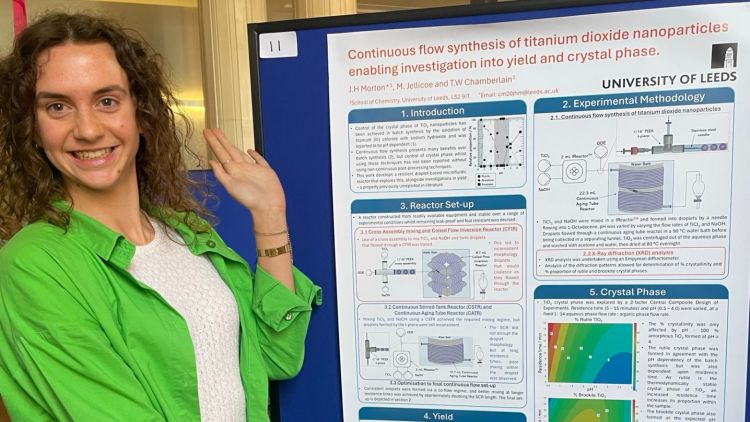 Jo wearing a green shirt pointing at her research poster