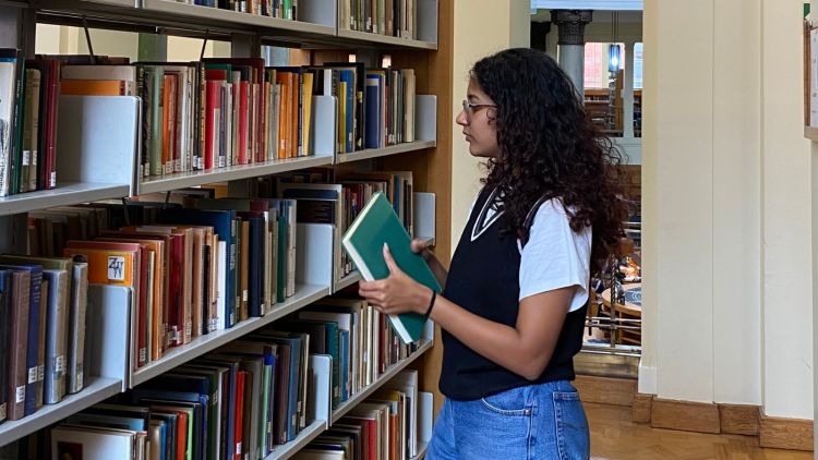 Female student looking at a bookshelf in the library, she is holding a book