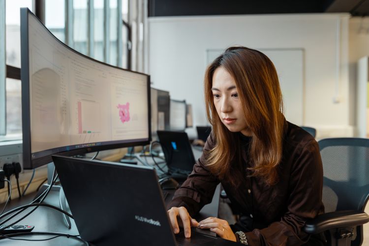 Female student looking at a laptop with data visualisations on a computer screen next to her