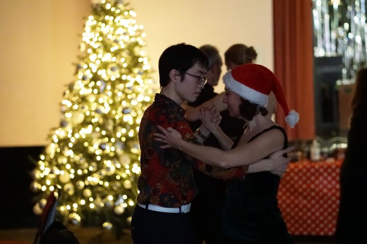 Muyou Li and a female student are dancing an argentine tango in front of a christmas tree