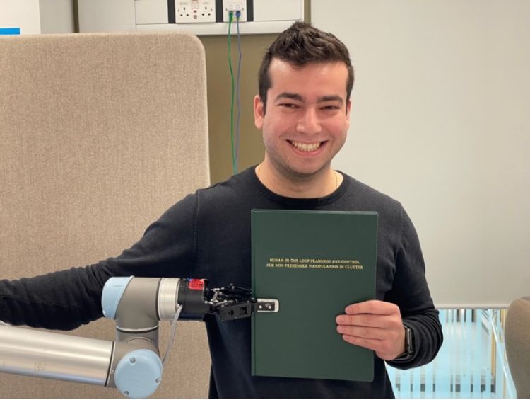 Image of Dr Rafael Papallas with the robot he used during his PhD, holding his PhD thesis