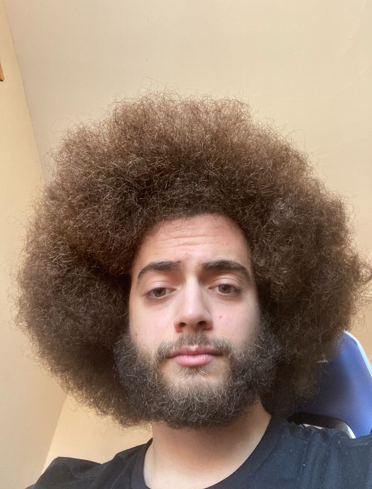 A photograph of Ryan Jamal with longer curly hair in an afro style.
