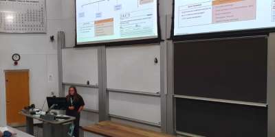 Female student giving a presentation of her research in front of a digital screen.