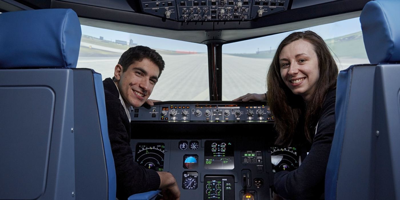 Students smiling as they sit in the flight deck of a simulator
