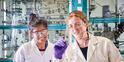 Two female researchers writing chemical formulas on a transparent screen