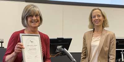 Professor ELaine Martin smiling while holding her award, a certificate in a frame