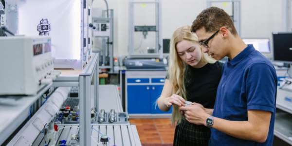 Two students using a piece of equipment in a workshop in the School of Electronic and Electrical Engineering.