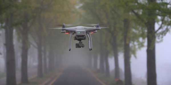 Image of a drone in the air, around a foggy road.