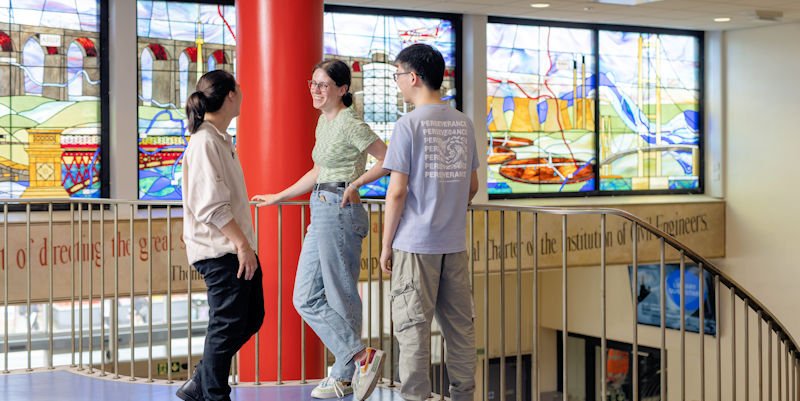 Students chat on Civil engineering staircase, with stained glass windows in the background